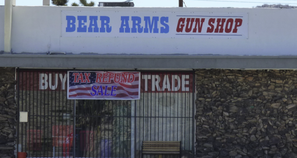 Storefront with the sign "Bear Arms Gun Shop" and a U.S. flag, security grill over its front.