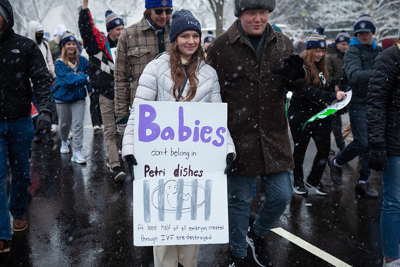 Woman holding sign "Babies don't belong in petri dishes. At least half of all embryos created for IVF are destroyed."