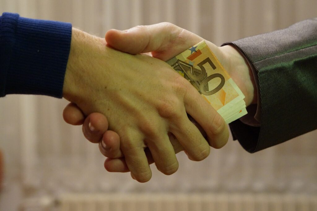 Article discusses corruption in E.U. countries. Image shows two people shaking hands, transferring a stack of 50 euro notes.